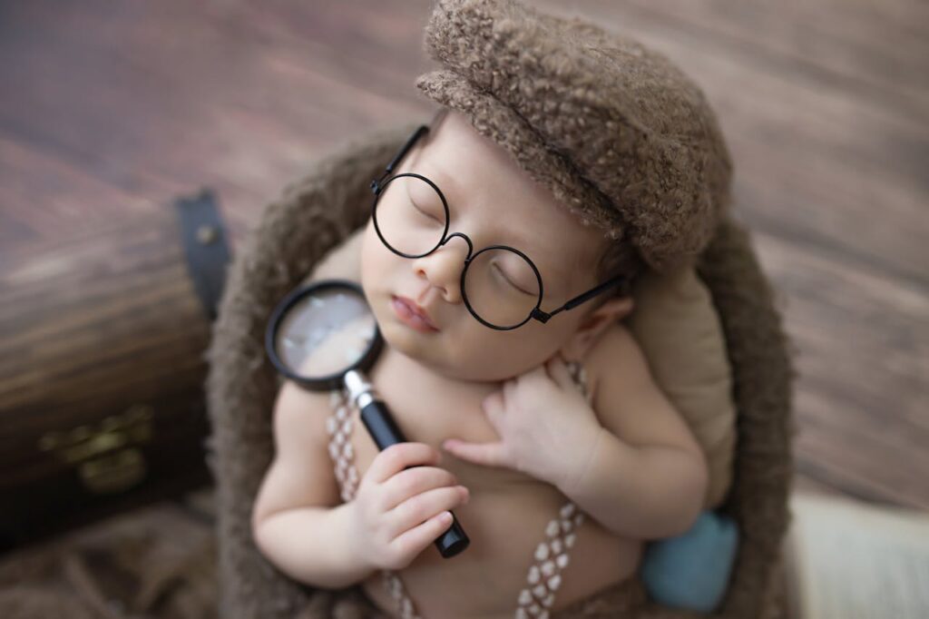 Cute baby sleeping with magnifying glass and glasses, wearing a hat.