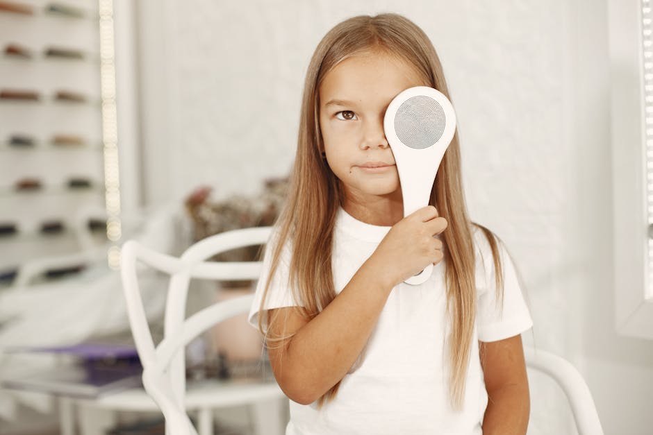 A young girl with long hair holding a magnifying glass over her eye in a bright indoor setting.